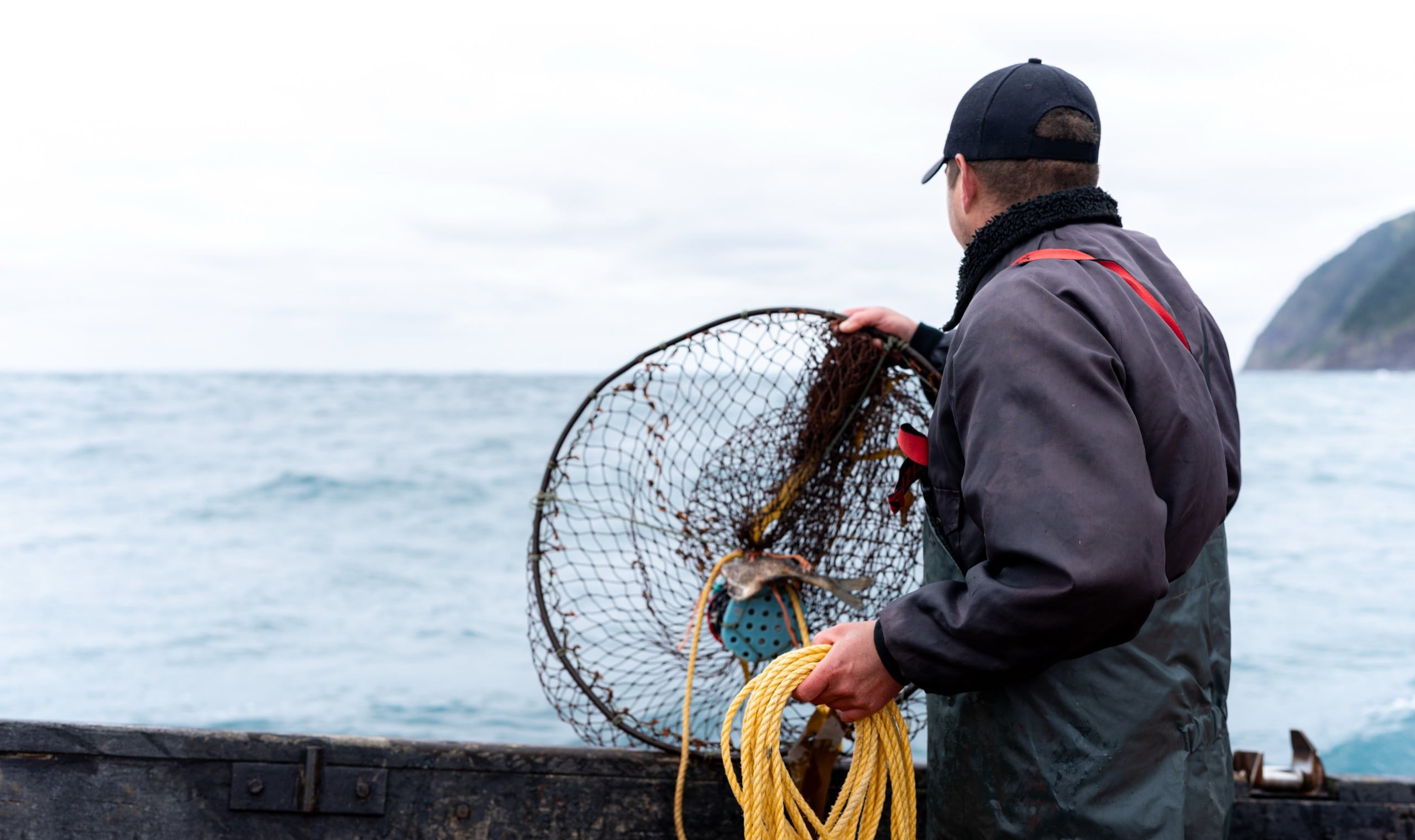 Rear view of a caucasian young fisherman picking up a container with nets for lobster fishing from the water